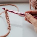 Dłoń z szydełkiem i różową włóczką podczas dziergania