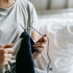 Kobieta siedzi na łóżku i dzierga z grubego sznurka bawełnianego