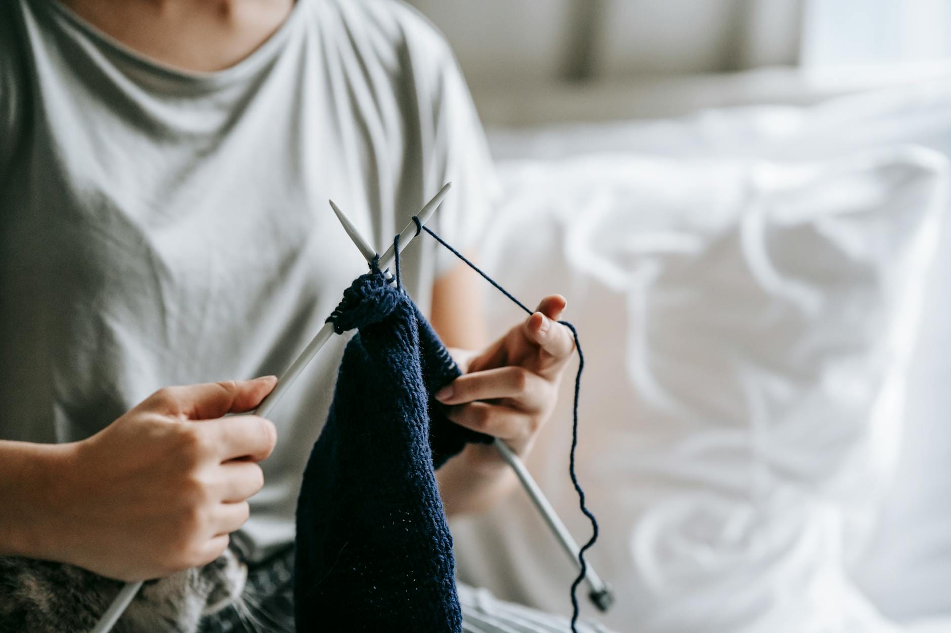 Kobieta siedzi na łóżku i dzierga z grubego sznurka bawełnianego