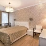 Sypialnia z łóżkiem małżeńskim, łóżeczkiem dziecięcym i dywanikiem przy łóżku