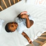 Uśmiechnięte niemowlę leży w łóżeczku, bawiąc się i patrząc w górę