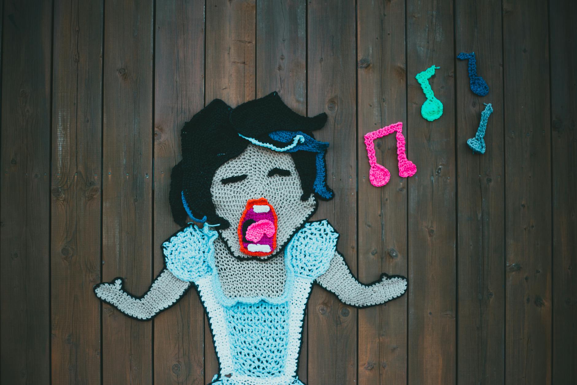 Kolorowy szydełkowy obraz śpiewającej kobiety z nutami na drewnie