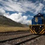 Niebieski pociąg na górskiej trasie kolejowej pod pochmurnym niebem