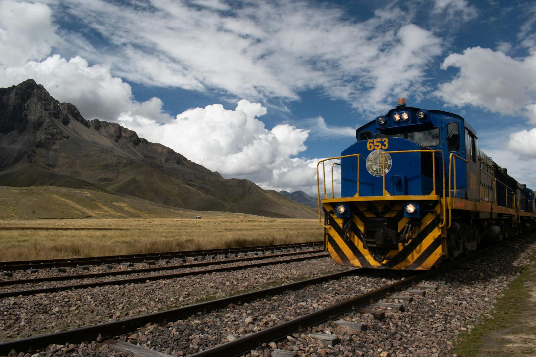 Jak przygotować się do podróży Koleją Transsyberyjską – praktyczny poradnik dla fotografów i miłośników dalekich wypraw Niebieski pociąg na górskiej trasie kolejowej pod pochmurnym niebem