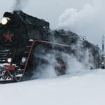 Zabytkowa lokomotywa parowa jedzie przez ośnieżony, zimowy krajobraz