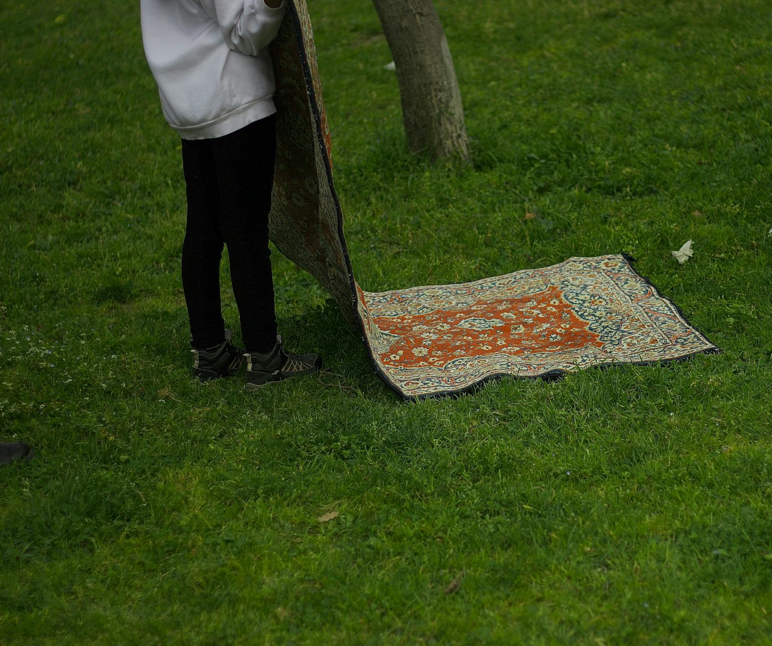 Osoba rozkłada kolorowy dywan handmade na trawniku na zewnątrz