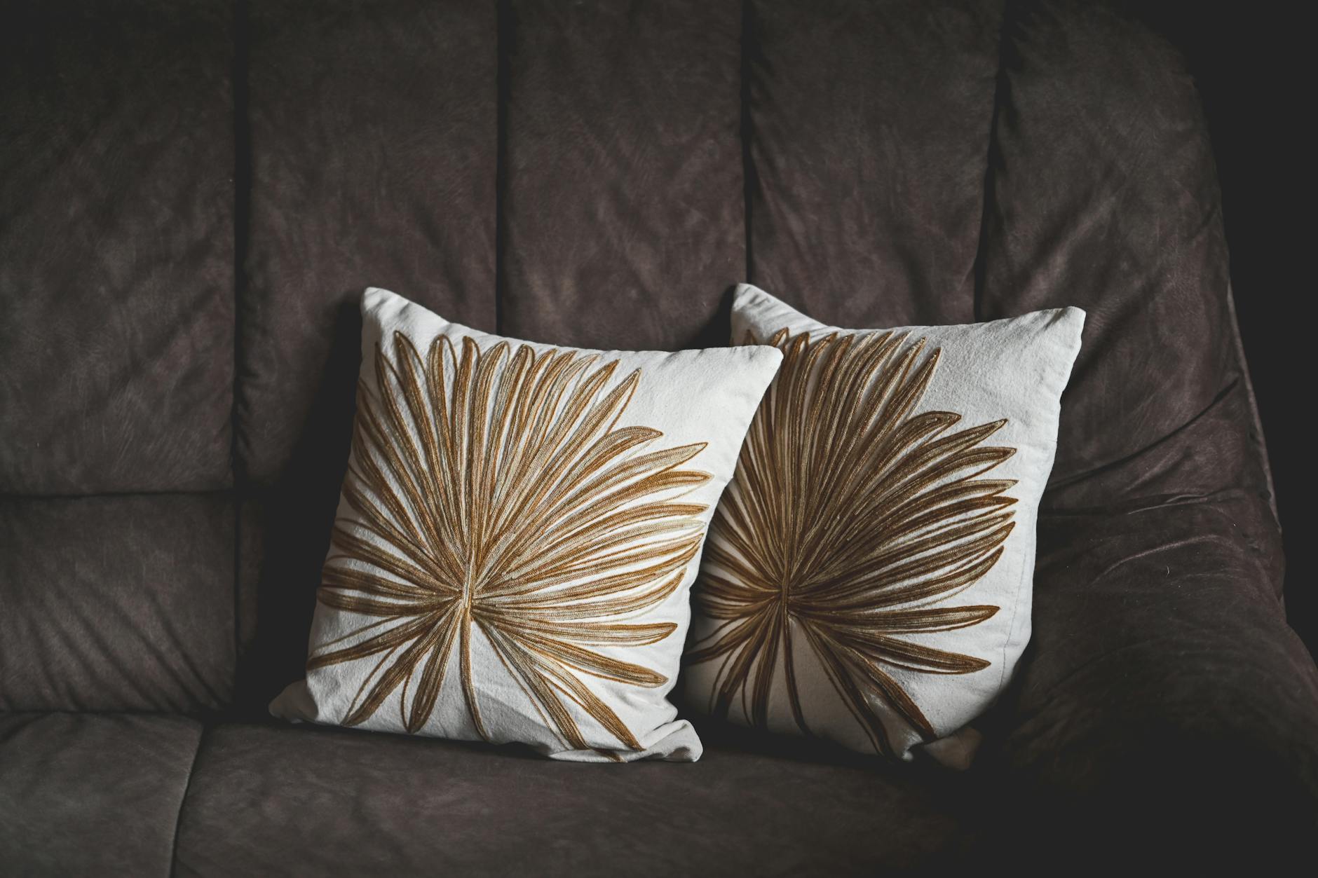 Poduszki z motywem liści na brązowej sofie w stylowym salonie